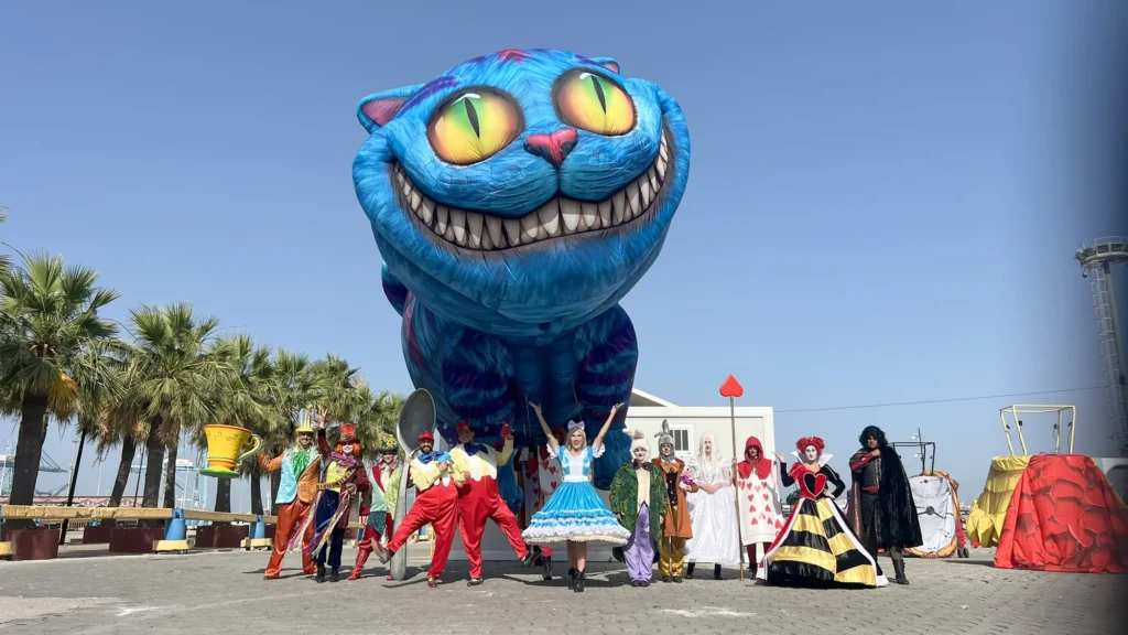 Elenco completo de Wonderland posando junto al Gato de Cheshire gigante en el puerto